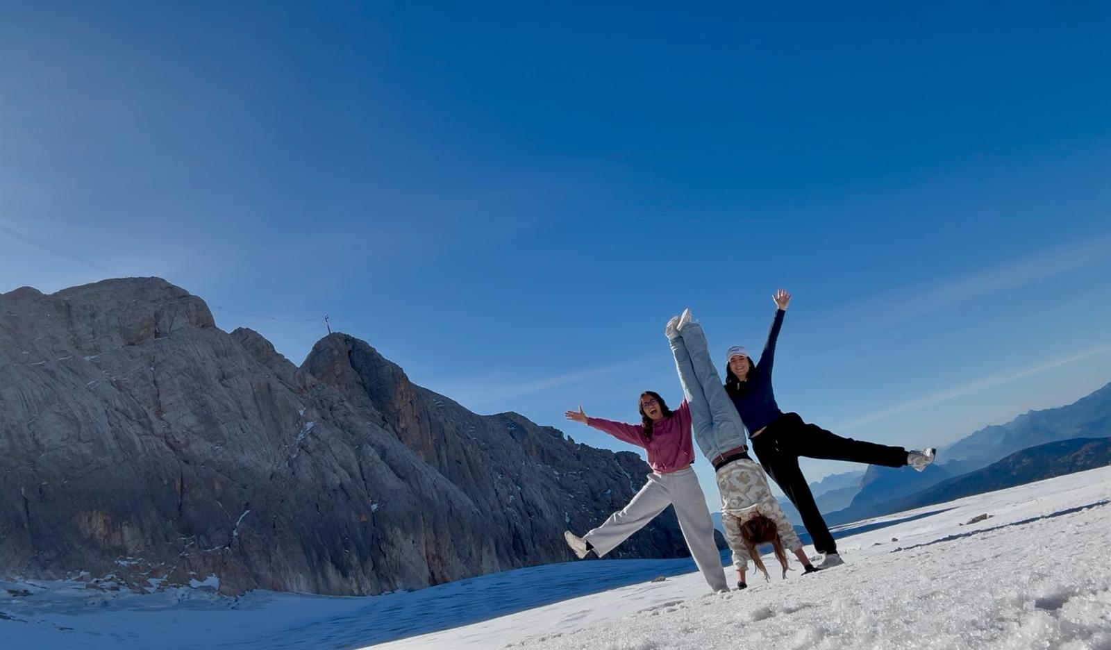 3 junge Frauen im Schnee machen Handstand vor Bergpanorma