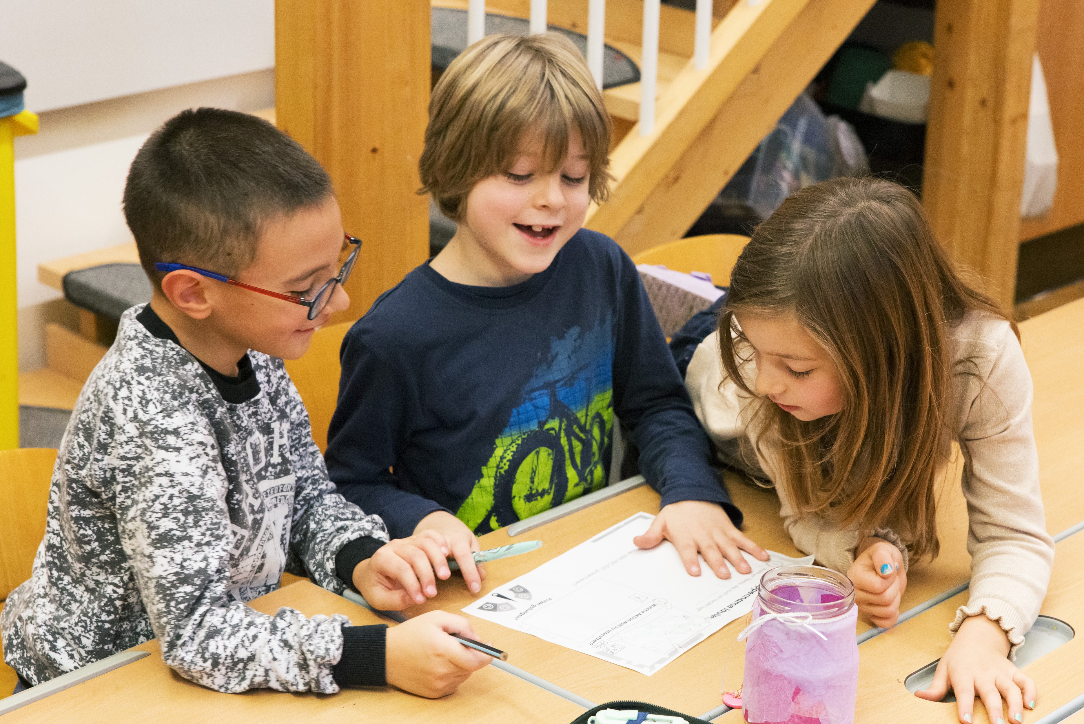 Drei Volksschulkinder um einen Tisch sitzend
