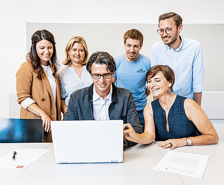 Personen versammeln sich um einen Laptop und schauen darauf 