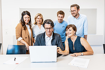 Personen versammeln sich um einen Laptop und schauen darauf 