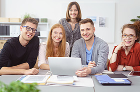 Symbolbild: 5 Studierende sitzen an einem Tisch mit Laptop und Lernunterlagen