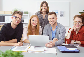 Symbolbild: 5 Studierende sitzen an einem Tisch mit Laptop und Lernunterlagen