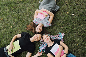 3 Jugendliche liegen im Gras