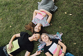 3 Jugendliche liegen im Gras