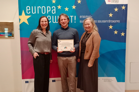 Zwei Frauen und ein Mann sthen vor einenm Plakat 