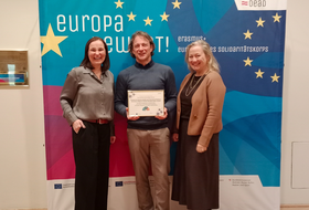 Zwei Frauen und ein Mann sthen vor einenm Plakat 