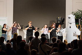 Mehrere Personen vor Publikum auf der Bühne beim Demonstrieren einer Station