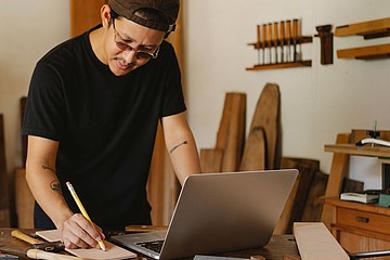 Handwerker in Werkstatt blickt auf Laptop