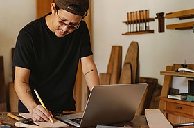 Handwerker in Werkstatt blickt auf Laptop