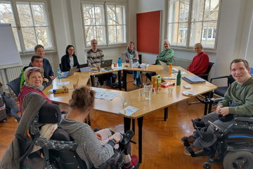 Personen sitzen am Tisch und lächeln in Kamera