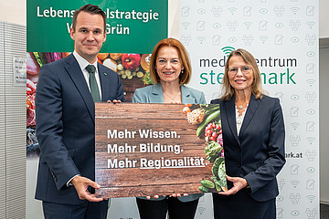 Zwei Frauen und ein Mann stehen nebeneinander und halten eine Tafel in ihren Händen