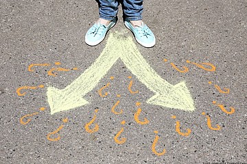 Füße auf Asphalt vor 2 Pfeilen und Fragezeichen