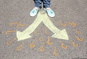 Füße auf Asphalt vor 2 Pfeilen und Fragezeichen