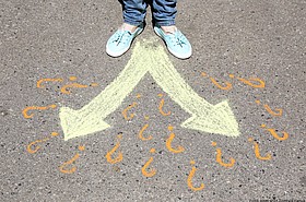 Füße auf Asphalt vor 2 Pfeilen und Fragezeichen