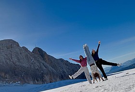 3 junge Frauen im Schnee machen Handstand vor Bergpanorma