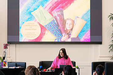 eine Frau steht auf der Bühne und spricht ins Mikrofon 