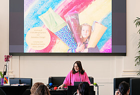 eine Frau steht auf der Bühne und spricht ins Mikrofon 