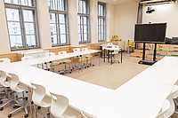 Ein heller Raum mit Tischen in U-Form angeordet, mit Bürostühlen herum und einer Interaktiven Tafel beim offenen Teil des U.