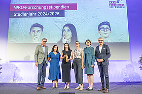 Viktoria Pauritsch mit Preis, Daniela Longhino, VR Elisabeth Amtmann und Vertreter WKO auf der Bühne, im Hintergrund Leinwand 