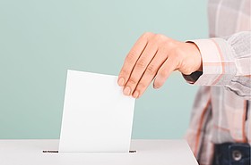 Hand steckt Wahlkuvert in Wahlurne