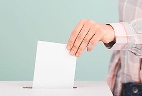 Hand steckt Wahlkuvert in Wahlurne