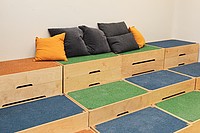 Bunte Holzstufen sind zu einer Sitztreppe zusammengestellt, Pölster liegen darauf