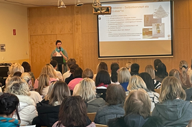 Personen sitzen im Publikum und bekommen Vortrag 